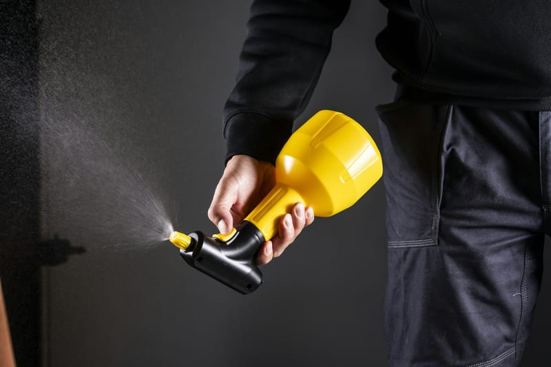 Aplicación profesional de insecticida con aspersora en el perímetro de una casa